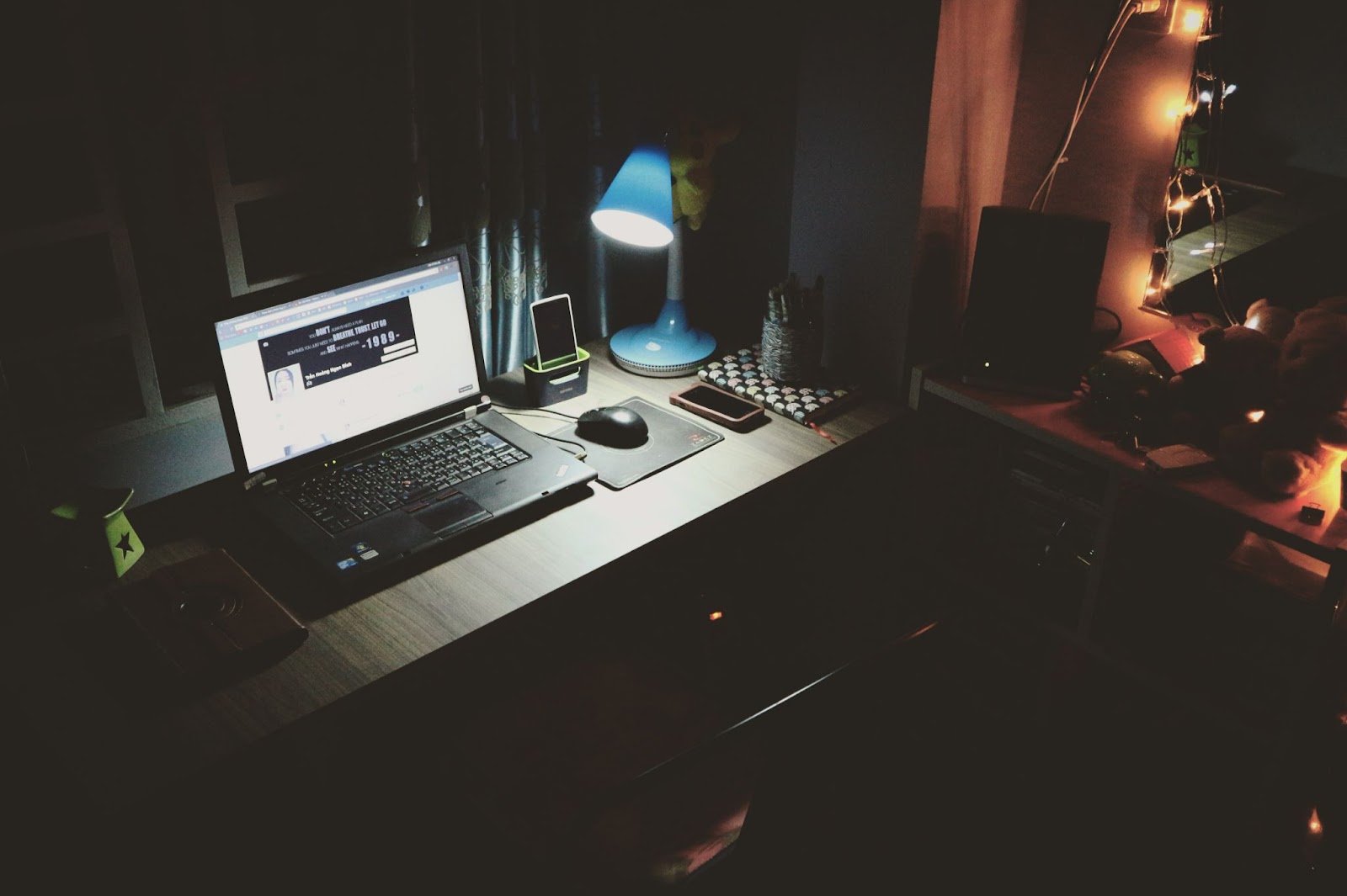A laptop and a phone on top of a desk, and a lamp shining on them